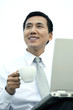 Businessman holding a cup while using laptop