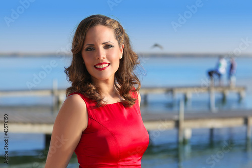 Photo: Brunette woman dress in red smiling relaxed on a lake Brunette woman dress in red smiling relaxed on a lake