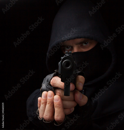 Photo: Masked robber with gun aiming into the camera Masked robber with gun aiming into the camera