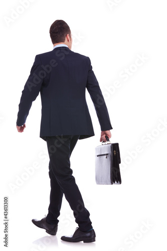 Photo: back of a walking business man holding a briefcase back of a walking business man holding a briefcase
