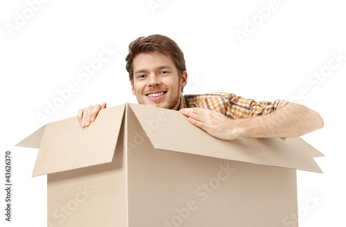 Photo: Pretty man hides inside the cardboard box, isolated Pretty man hides inside the cardboard box, isolated