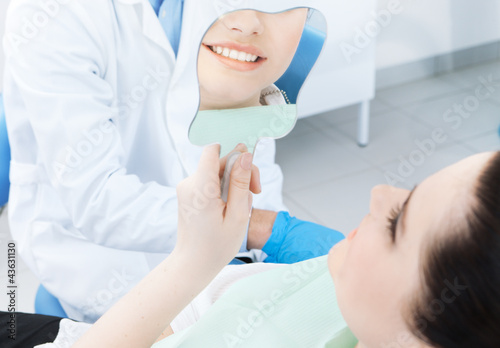 Foto: The patient admires her smile looking at the mirror The patient admires her smile looking at the mirror