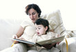 A woman sitting on the couch reading a book for her son