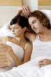 A couple lying on the bed reading newspaper