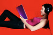 A lady with a headphone covering her ears lying on the couch reading a book