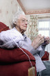 An old bespectacled woman sitting on the couch knitting