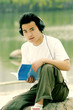 Foto: A man sitting on the lakeside listening to music on his headphone while reading book A man sitting on the lakeside listening to music on his headphone while reading book