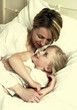 A woman hugging her daughter who is lying on the bed