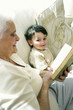 Photo : An old woman sitting on the couch reading book while her grandson is sitting beside her An old woman sitting on the couch reading book while her grandson is sitting beside her