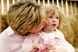 A woman kissing her young daughter who is sitting on her lap