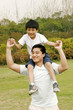 A man giving his son a piggy back ride in the park