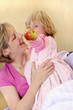 A young girl standing beside her mother holding a red apple