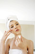 Foto: A woman with her hair and body wrapped up in towel applying under eye cream A woman with her hair and body wrapped up in towel applying under eye cream