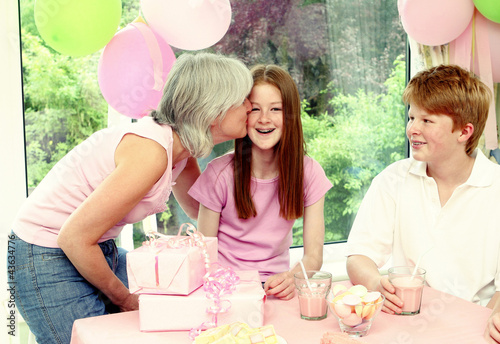 Photo: A woman giving her daughter a birthday kiss while her son watching A woman giving her daughter a birthday kiss while her son watching