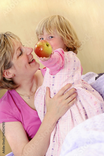 Photo: A young girl standing beside her mother holding a red apple A young girl standing beside her mother holding a red apple