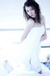 A woman with wet hair and body wrapped up in towel kneeling on the bed