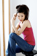 A lady in red spaghetti top and jeans sitting on a stool