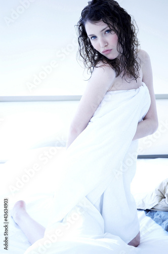 Photo: A woman with wet hair and body wrapped up in towel kneeling on the bed A woman with wet hair and body wrapped up in towel kneeling on the bed