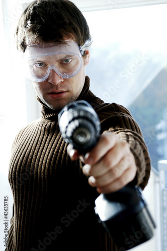 Photo: Man with goggles pointing a drill at the camera Man with goggles pointing a drill at the camera
