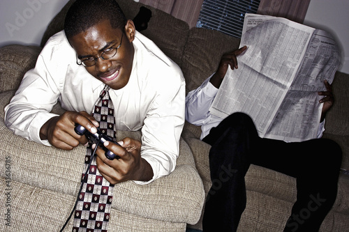 Photo: Businessman playing video game console while his friend is reading newspaper Businessman playing video game console while his friend is reading newspaper