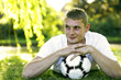Teenage boy lying forward on the field hugging a soccer ball