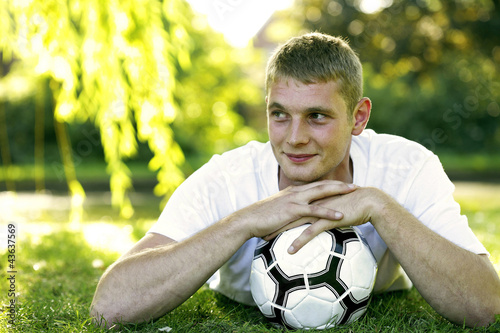Photo: Teenage boy lying forward on the field hugging a soccer ball Teenage boy lying forward on the field hugging a soccer ball