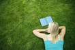 Teenage girl lying forward on the field with book in front of her