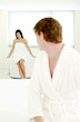 Man in bathrobe sitting on bed with his girlfriend sitting on the bathtub
