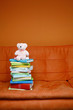A stack of books and a teddy bear on the couch