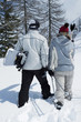 Rear view of couple walking away from camera, holding winter sport equipments