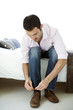 Man sitting on bed tying his shoelace