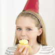 Girl in party hat eating cupcake