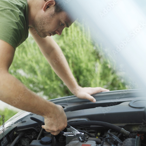 Photo: Man looking under car hood, fixing car with pliers Man looking under car hood, fixing car with pliers