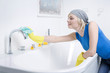 Woman with rubber gloves, cleaning the faucet