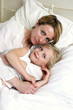 A short hair woman lying on the bed hugging her daughter