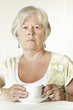 Thoughtful Senior lady sitting at table holding a cup of tea