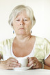 Thoughtful Senior lady sitting at table holding a cup of tea