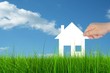 Conceptual white house held in hand in green grass