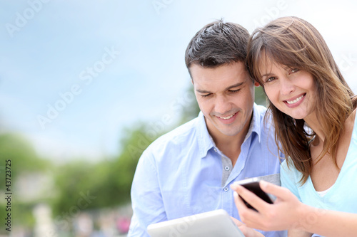 Photo: Couple using tablet and cellphone in public park Couple using tablet and cellphone in public park