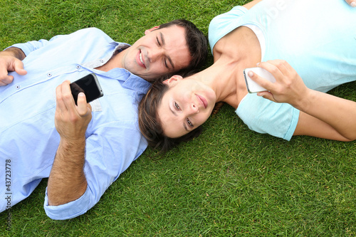 Foto: Couple relaxing in grass while using smartphone Couple relaxing in grass while using smartphone