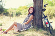 Beautiful girl sitting near bike and tree at rest in forest. Pho