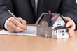 Foto: Businessman signs contract behind house architectural model Businessman signs contract behind house architectural model