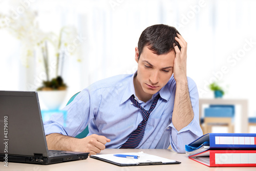 Photo: Young desperate businessman in his office looking down Young desperate businessman in his office looking down