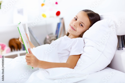 Photo: Girl with a book in bed at home Girl with a book in bed at home