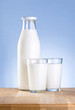 Full Bottle of fresh milk and two glass is wooden table on a blu