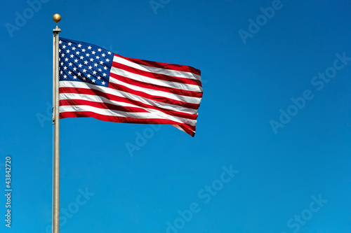 Photo: US American flag waving in the wind with beautiful blue sky in b US American flag waving in the wind with beautiful blue sky in b