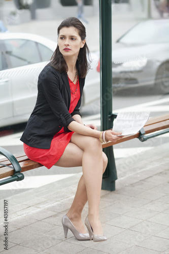 Photo: Woman waiting at the bus stop and holding a newspaper Woman waiting at the bus stop and holding a newspaper
