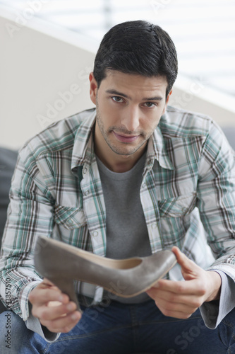 Photo: Man sitting on a couch and holding a high heel shoe Man sitting on a couch and holding a high heel shoe