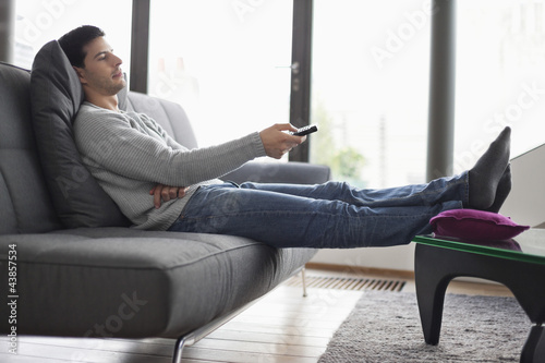 Photo: Man reclining on a couch and watching television Man reclining on a couch and watching television