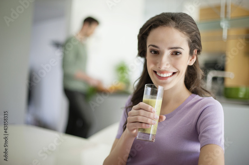 Photo: Woman drinking soup with her husband preparing food in the background Woman drinking soup with her husband preparing food in the background
